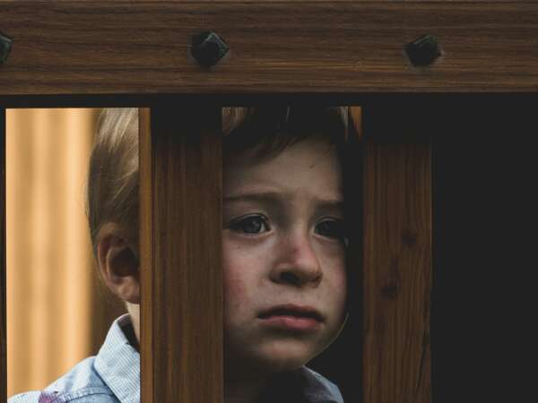 A boy with a sad face next to some wooden railings