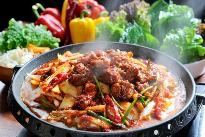 Steaming spicy Chinese dish with vegetables in the background