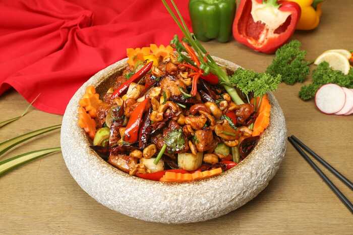 Kungpao-chicken in a stone plate bowl with some vegetables in the back