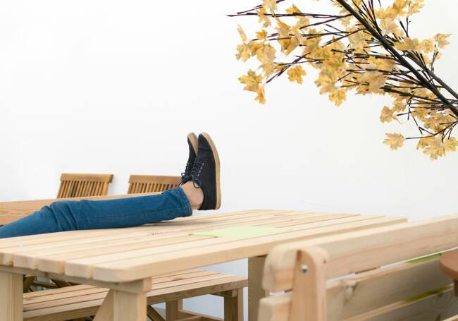 A person relaxing by a wooden table-chair set, with her feet placing on the table